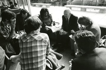 Black and white photo of James Coleman speaking with a small group of reporters