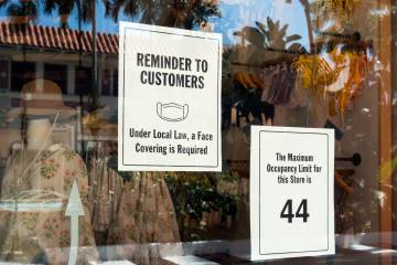 A sign requiring masks and stating an occupancy limit is displayed on a shop window