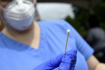 A nurse holds out a nasal swab for COVID-19 testing