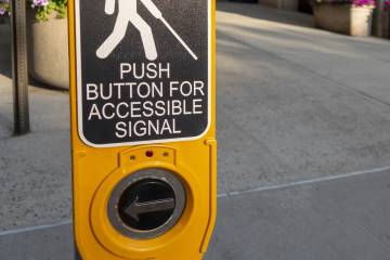 Photo of a city crosswalk sign featuring Braille that states, “Press button for accessible signal.”