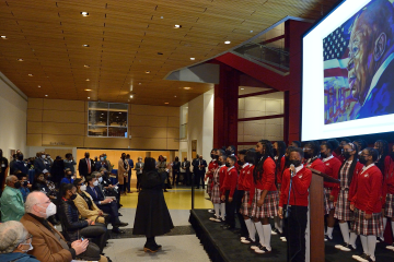 A children's choir performs on a low stage as Elijah Cummings' portrait is projected on a screen behind them