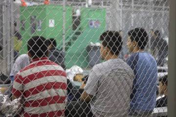 Three boys sit with their back to a chain-link fence at a detention center