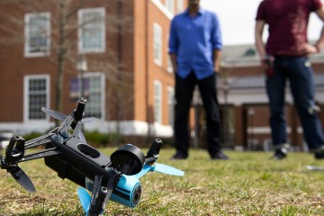 Two students stand in the background while a drone sits in the foreground
