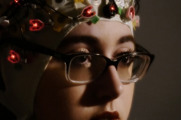 A close-up of a woman's face while she wears what looks like a swimming cap with blinking lights and attachments to it