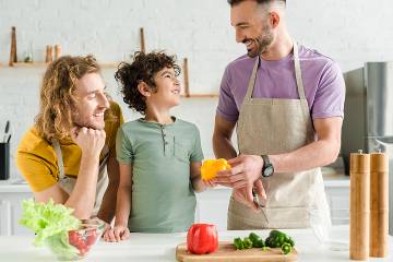 Two dads and their young son cutting up peppers in the kitchen