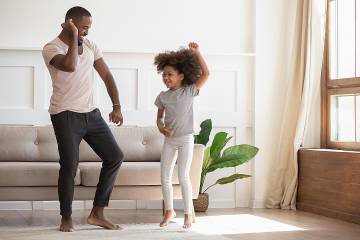 Man and daughter dancing energetically in the living room