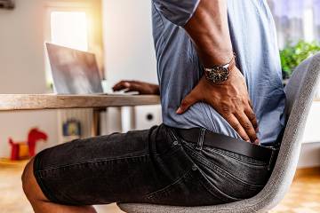 Man sitting at desk with hand on sore lower back