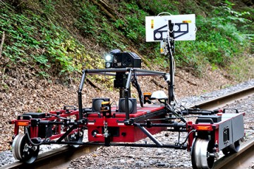 The robot spans across railroad tracks on a metal frame and is equipped with cameras and sensors