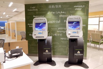 Two computer kiosks in from of dark green wall with words in various languages