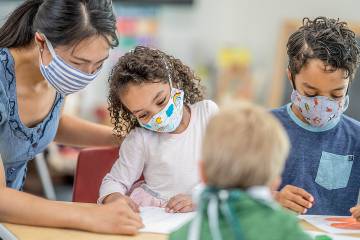 Masked woman and three children working at a table