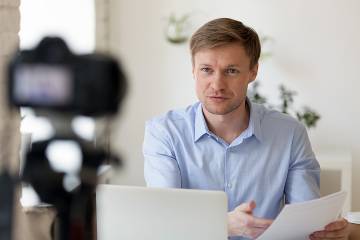 Man at desk facing laptop and camera