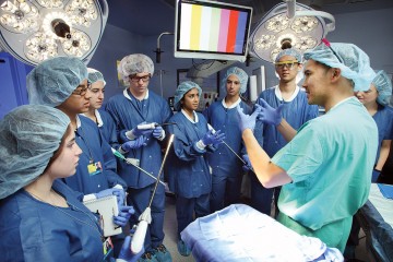A physician in scrubs instructs a group of undergrads