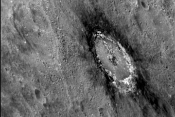 A black and white image of a crater in Mercury's surface, surrounded by dark marks at the rim of the crater.