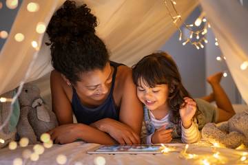Mother and daughter using digital tablet inside illuminated cozy hut