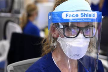 A nurse looks directly into the camera while wearing an N-95 mask and plastic splash shield