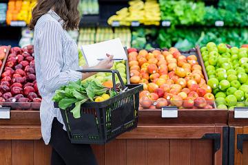A woman in the grocery store fills her hand basket with produce
