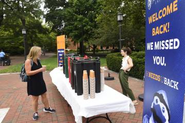 Two women smile over coffee in front of Levering Hall