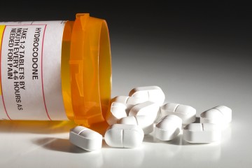 Orange prescription bottle labeled 'hydrocodone' with white pills spilling out 