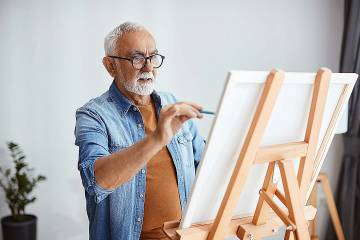 Senior man painting on a canvas on an easel in his home studio