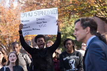 A student protester holds a sign that reads 'JHU stands with Mizzou, Yale, Howard, Claremont McKenna, VCA, Ithaca, Bowie State, USC'
