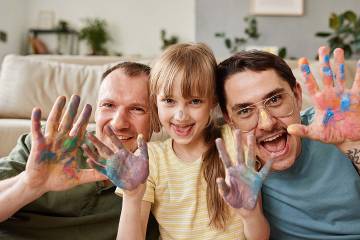 Smiling young girl and her two dads showing their paint-covered hands