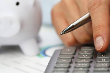 Hand on calculator with piggy bank in background