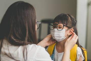 Mom prepares young child with face mask and backpack for school