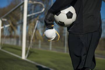 A man holds a soccer ball and a mask on a soccer field 