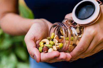 A hand holding nuts pouring from a jar