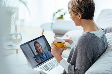 A woman sitting in bed with her laptop confers with a doctor on the screen