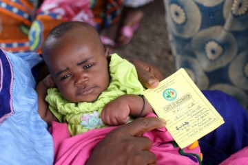 Baby held by parent who also holds a vaccination card