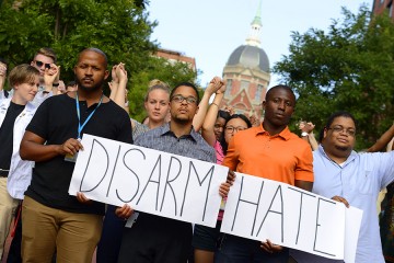 Vigil attendees hold a sign that reads 'Disarm Hate;' the Johns Hopkins Medicine dome can be seen in the background