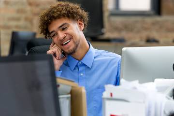 Young man working in office surrounded by to monitors and many files