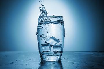 Water splashes out of a glass as ice cubes are dropped into it