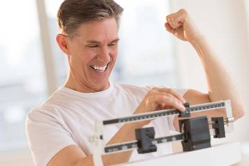 Mature man clenching fist excitedly while using balance weight scale at gym
