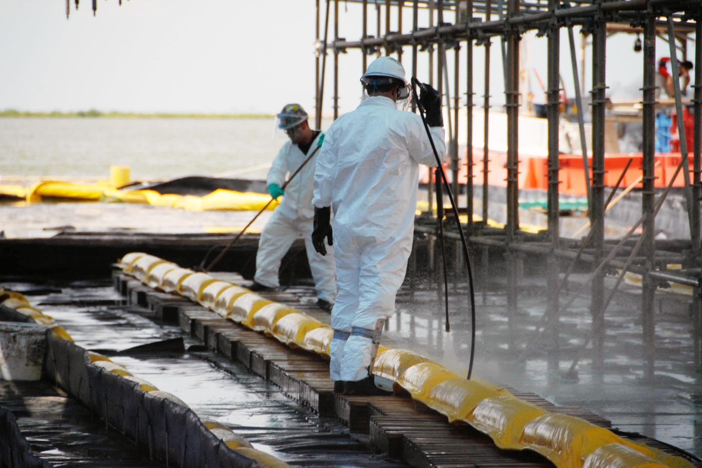 Workers in protective suits hose down a large yellow inflated hose used to contain the oil spill