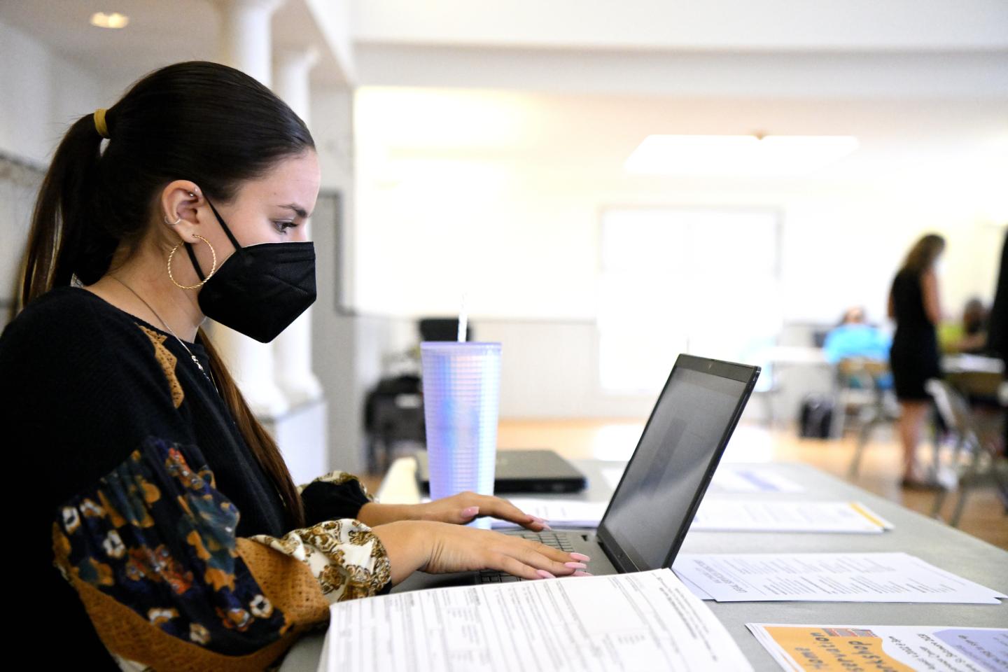 A person, wearing a mask, works at a computer