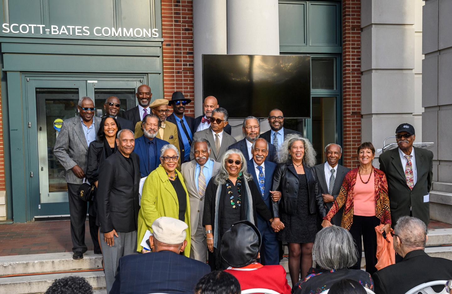 A group of about 20 people pose for a photograph in front of Scott-Bates Commons