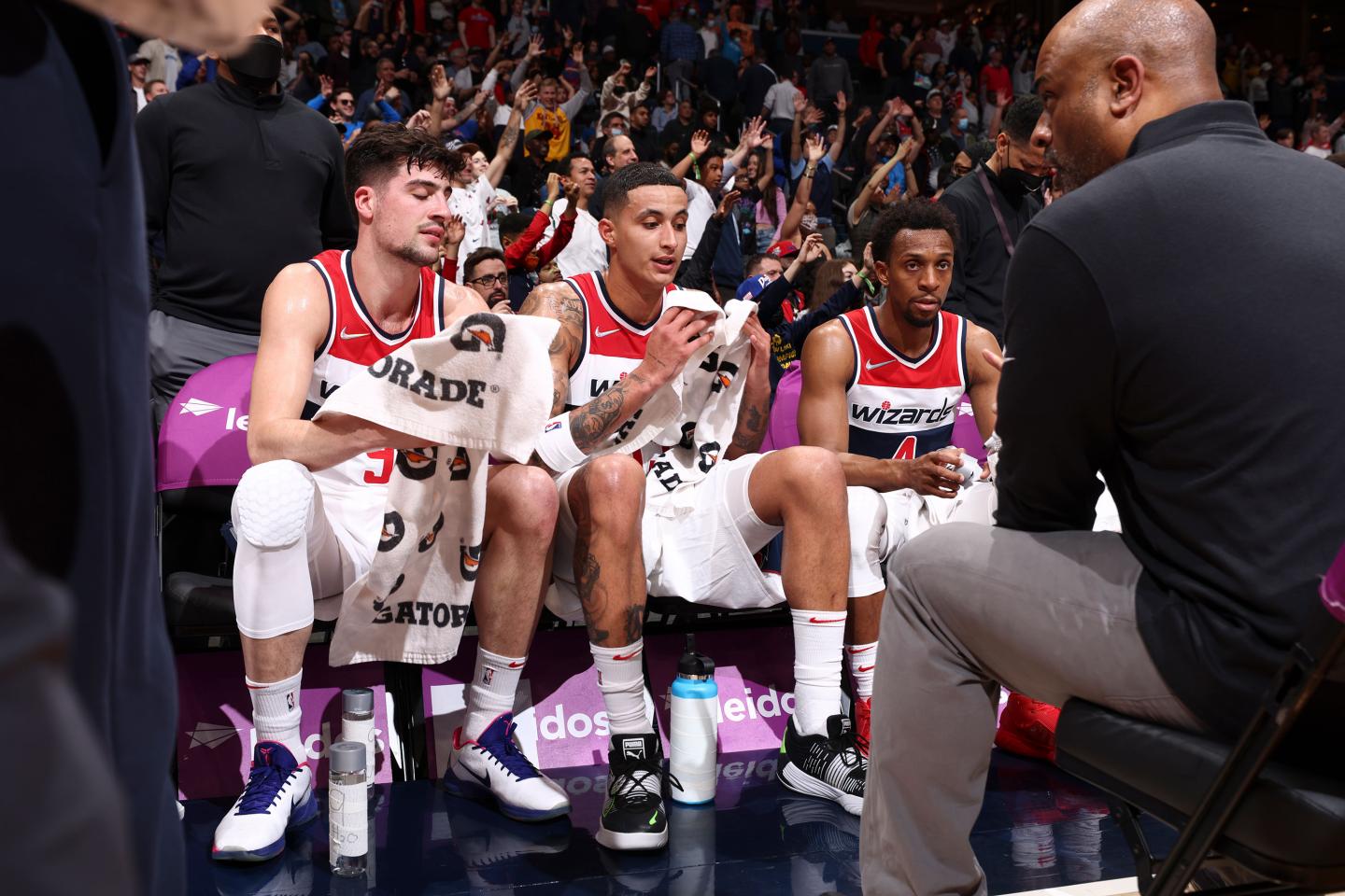 Wes Unseld Jr. sits and talks to players who are sitting on a courtside bench