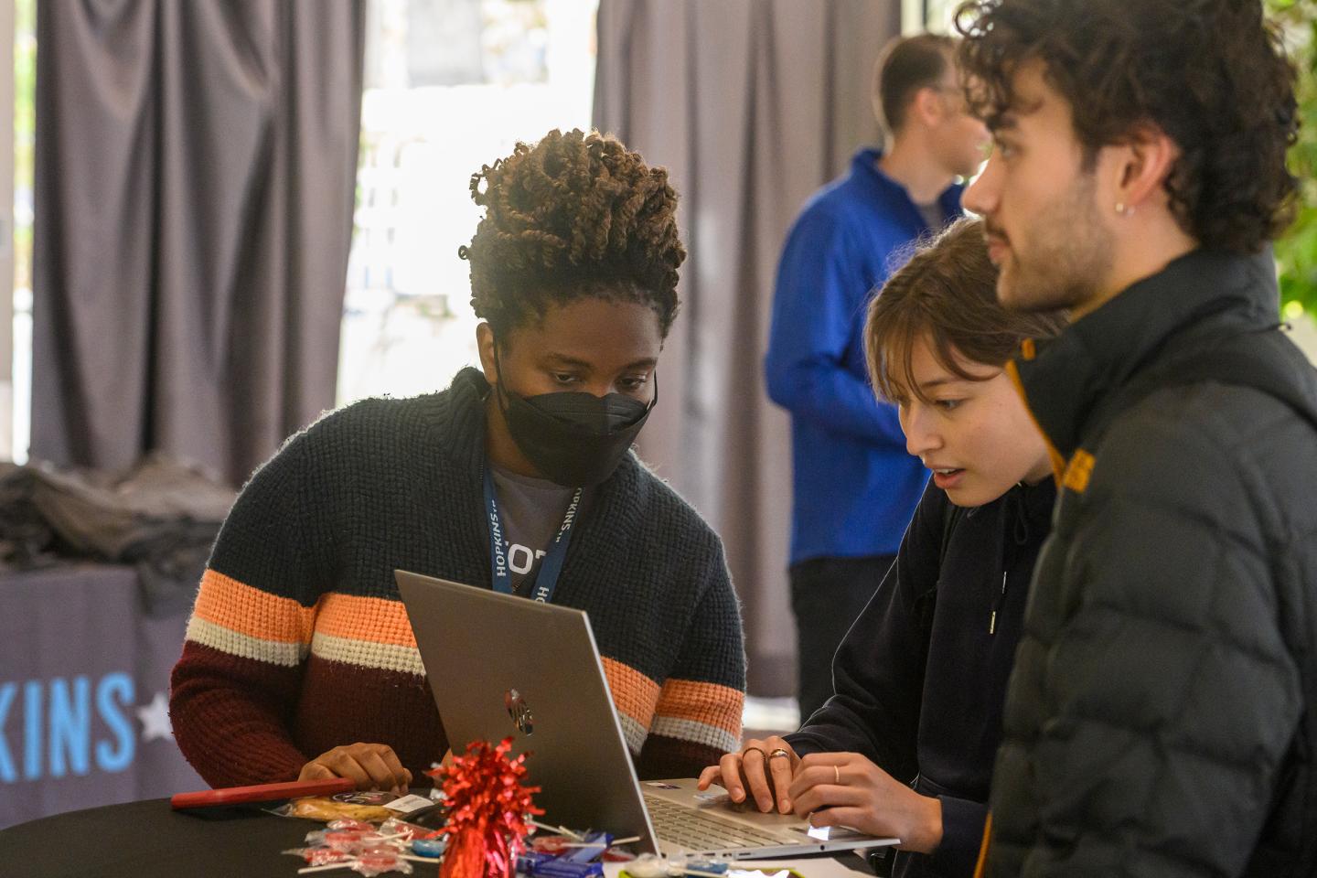 A student assists two others on a laptop