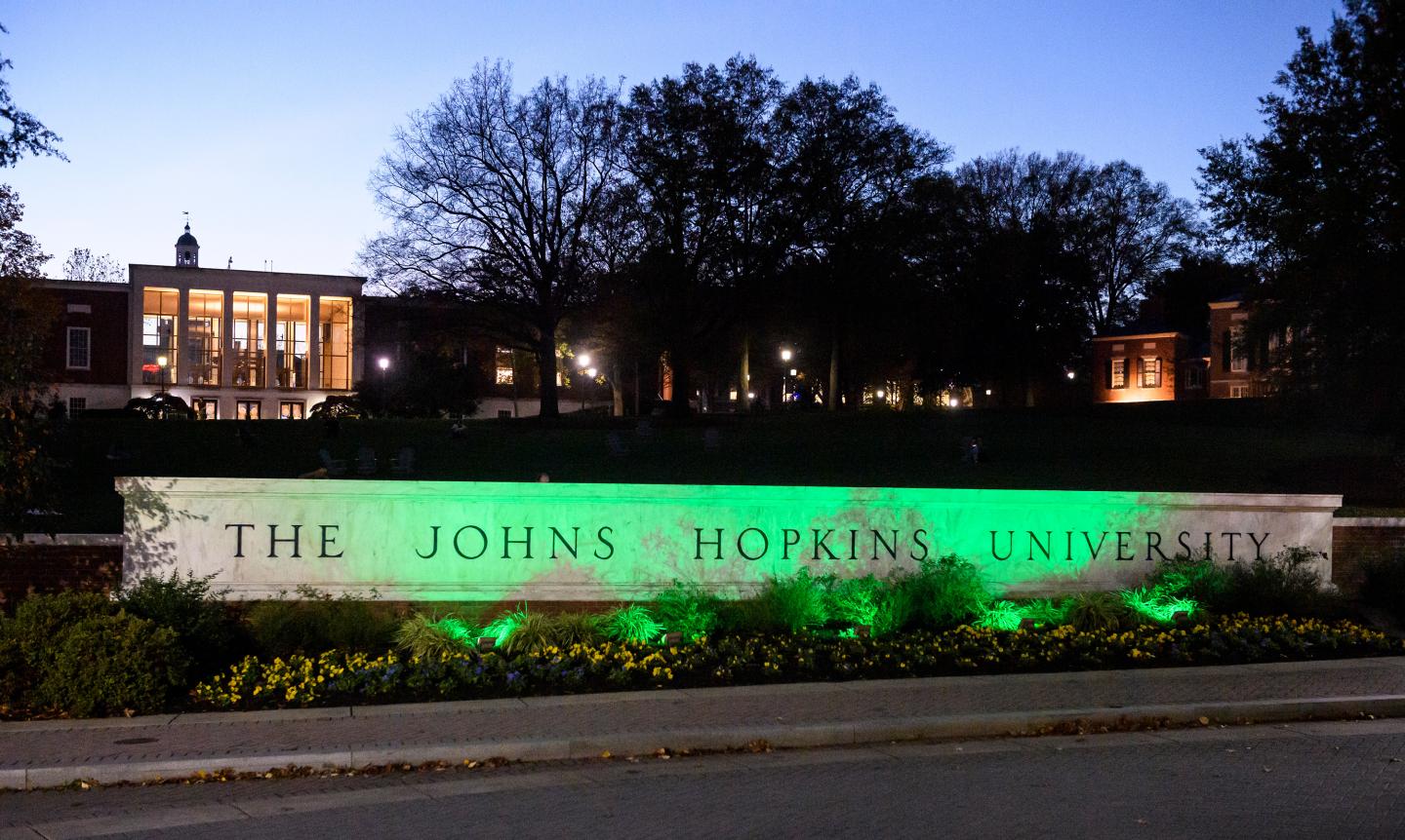 The Johns Hopkins University sign is bathed in green light at sunset