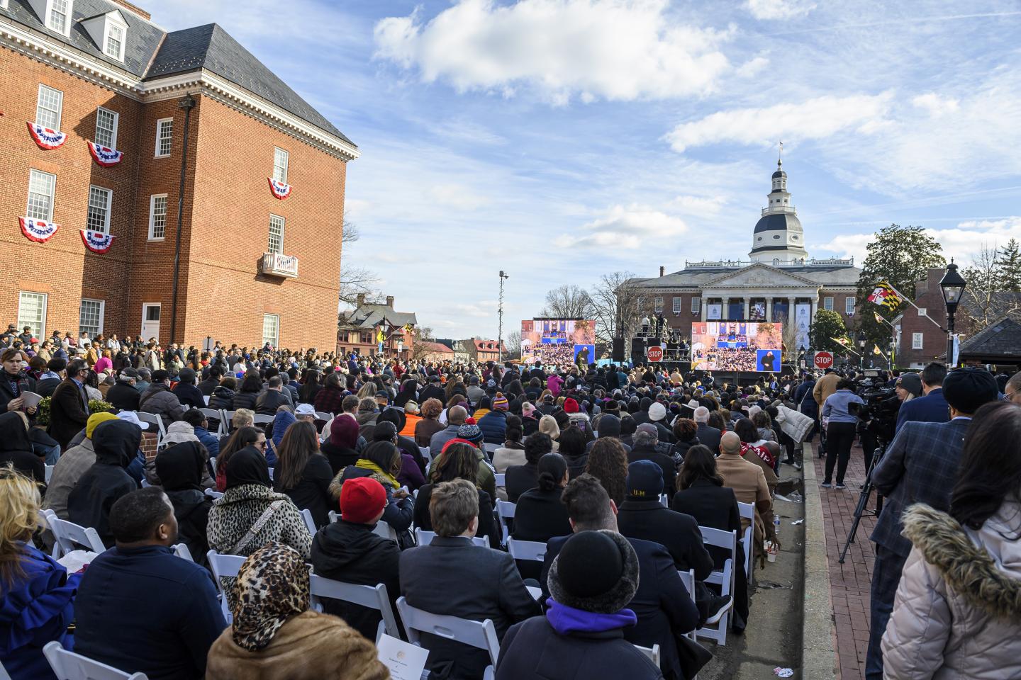 A large crowd gathers outdoors under blue skies in Annapolis for the inauguration of Governor Wes Moore