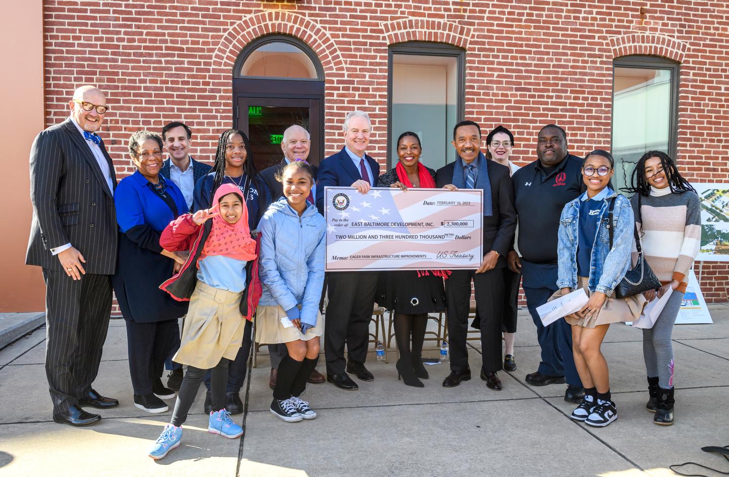 A group of 14 people - elected officials, students, and others - pose with a novelty check for $2.3 million