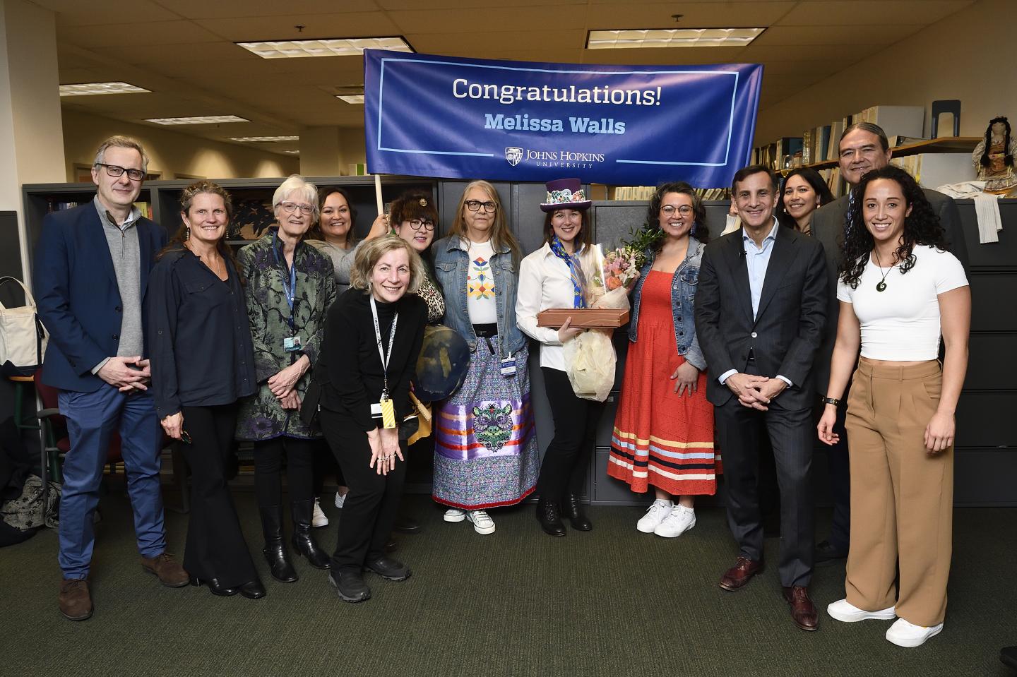 A group of people pose for a photo with a banner that readers 