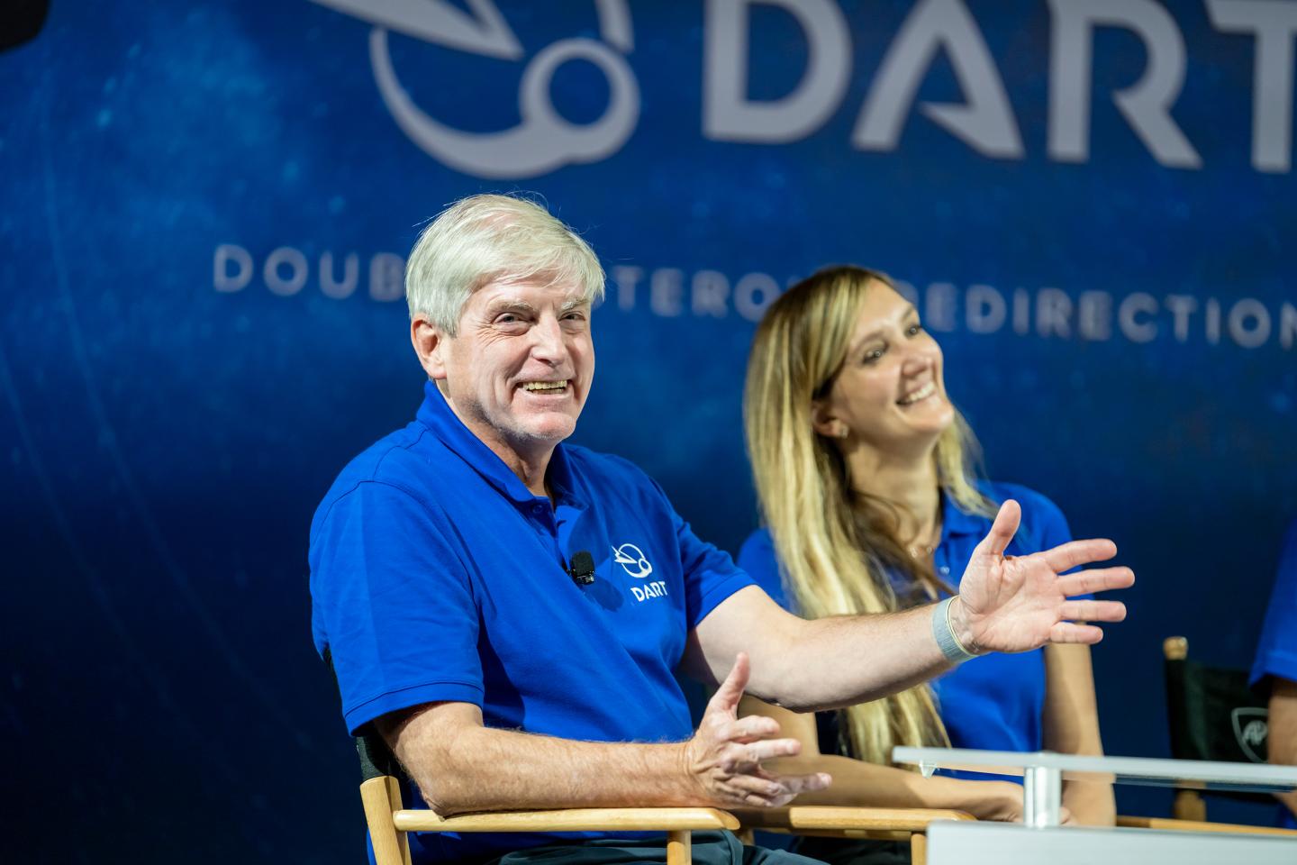 A man in a blue shirt is seen sitting in front of a large blue backdrop that reads DART