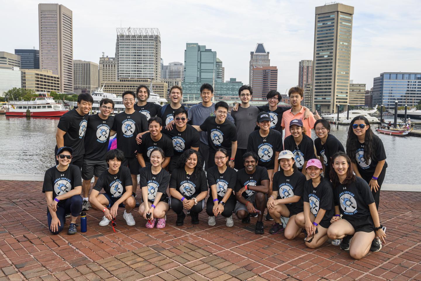 The JHU Dragon Boat Team smiles for a picture in front of Baltimore's Inner Harbor