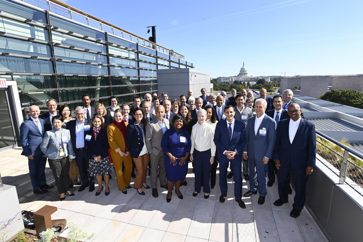 A large group of people pose for a photo on the roof, the U.S. Capitol visible in the background