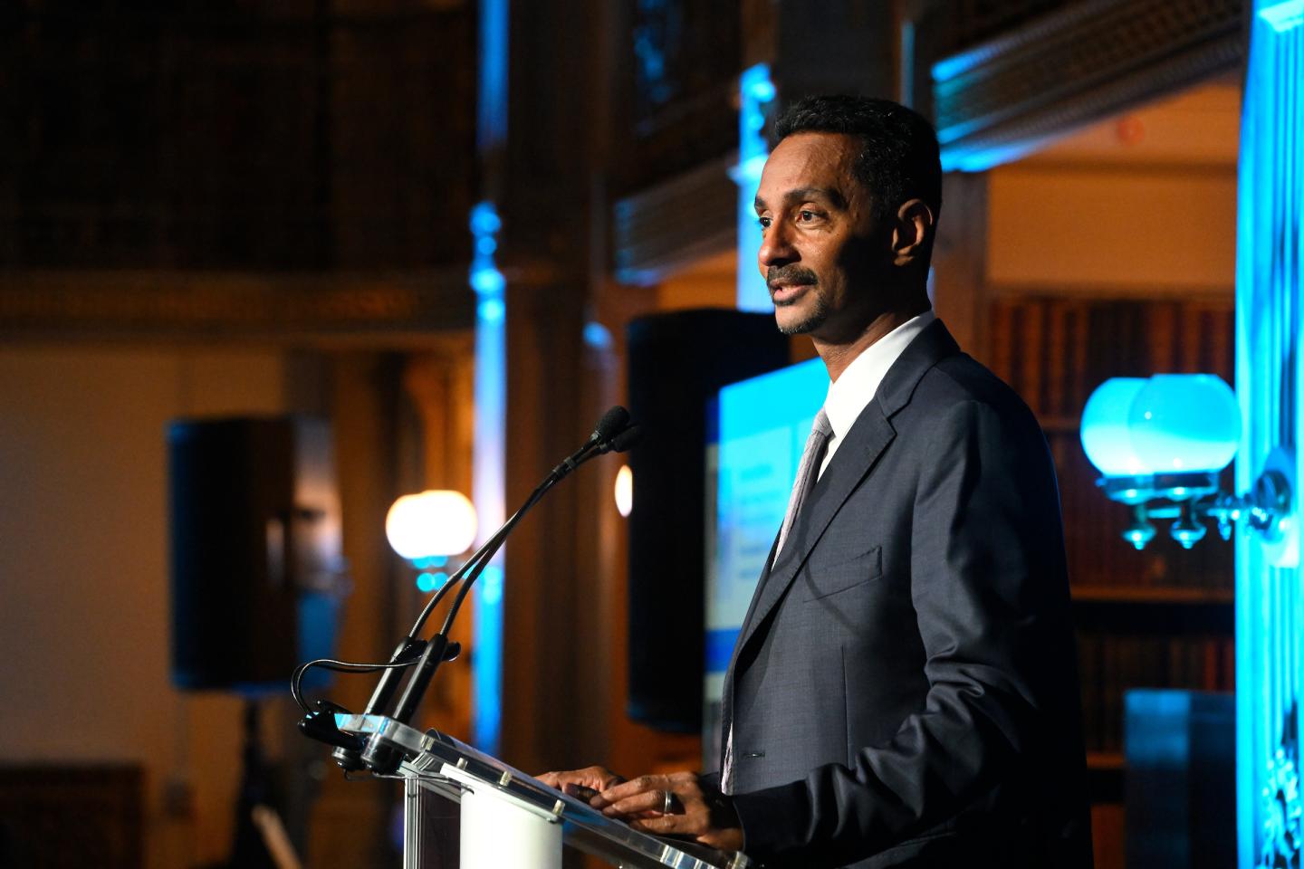 An adult in a suit speaks at a podium.