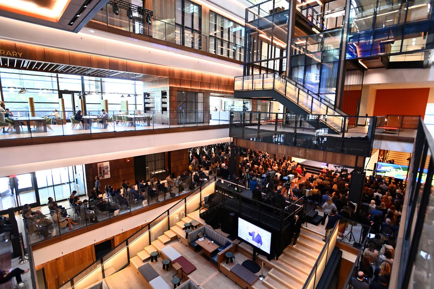 A large crowd is seated in the multistory atrium of a modern building