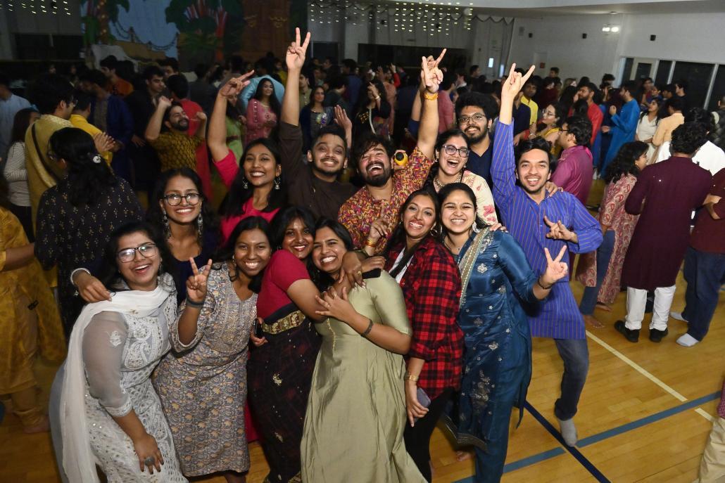 A group of 13 students dressed in Indian clothing smile for the camera on a dancefloor.